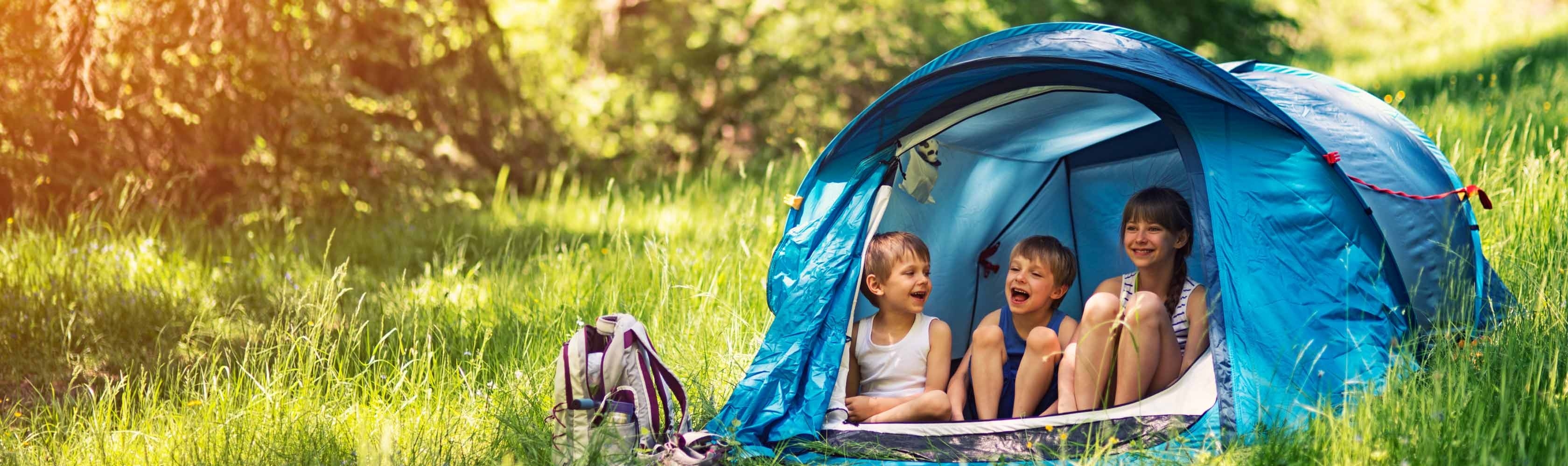 Hitzeferien – drei Kinder in einem blauen Zelt im Wald