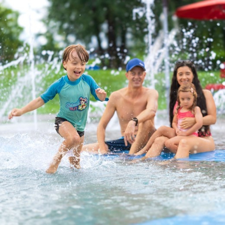 Badi-Tour 2026 – Mutter und Vater passen auf Kinder am Kinderbecken auf, Junge spielt im seichten Wasser.