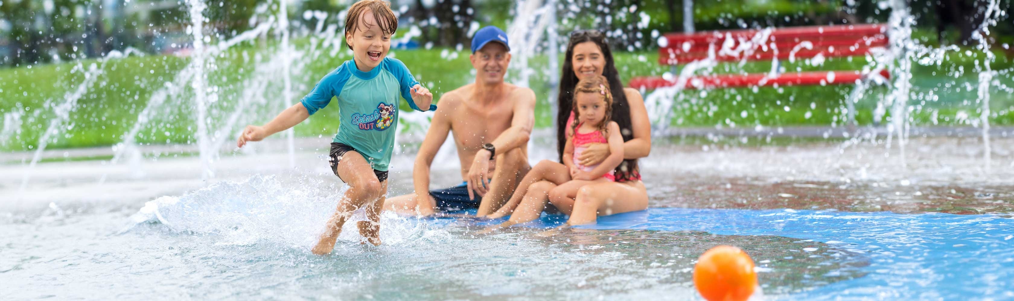 Badi-Tour 2025 - Mutter und Vater passen auf Kinder am Kinderbecken auf, ein Junge spielt im seichten Wasser.