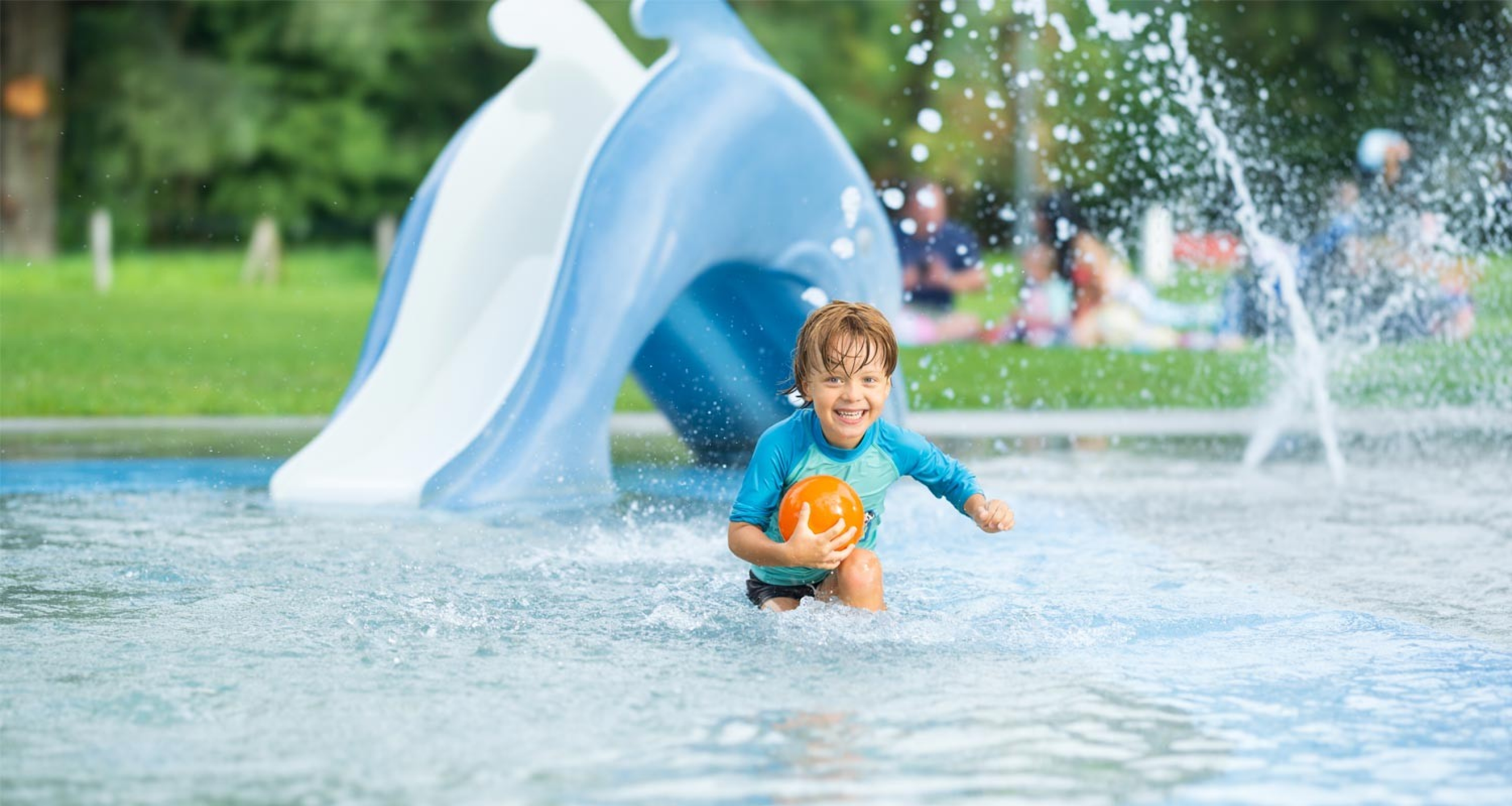 Badi-Tour 2025 - Ein Junge spielt in seichtem Wasser mit einem CONCORDIA-Ball, er rennt auf die Kamera zu.