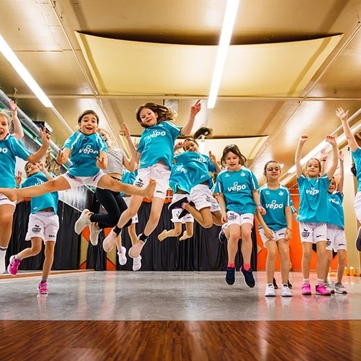 MS Sports - Bambini in maglia blu partecipano con entusiasmo a un evento sportivo in una sala, accompagnati da allenatori.