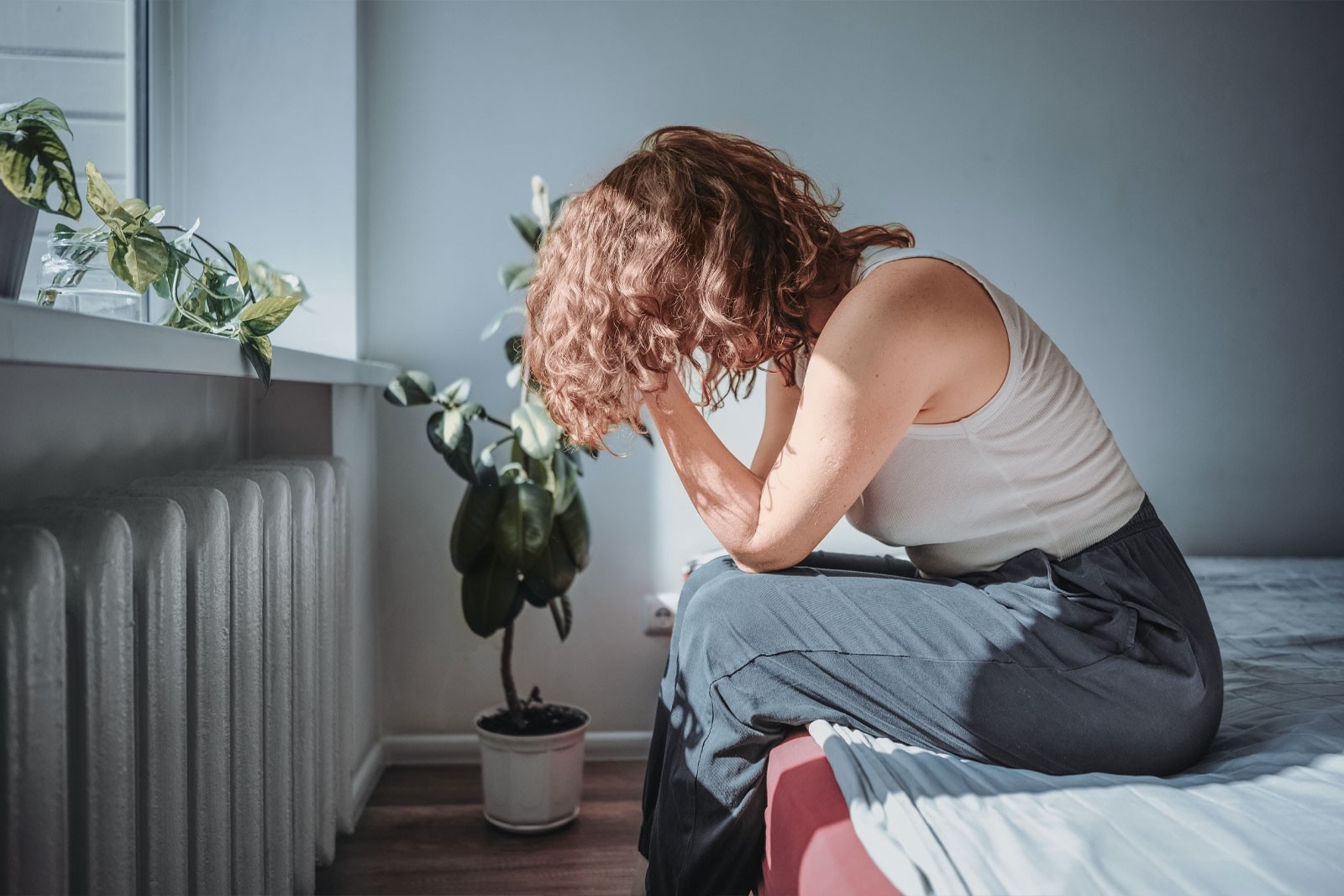 Postpartale Depression – Mutter sitzt auf dem Bett und stützt ihren Kopf mit den Händen