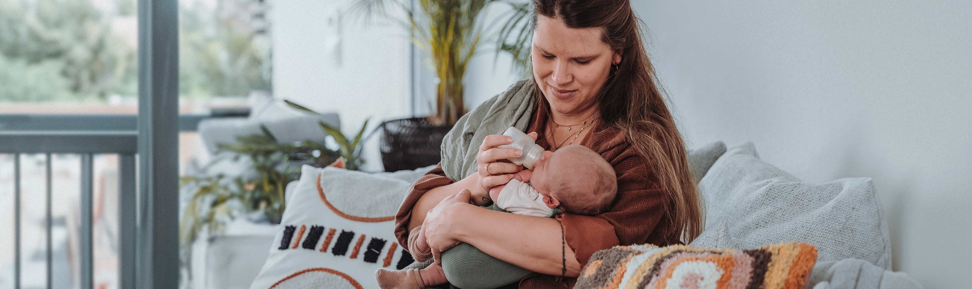 Wochenbett – Frau sitzt auf dem Sofa und gibt ihrem Baby die Flasche