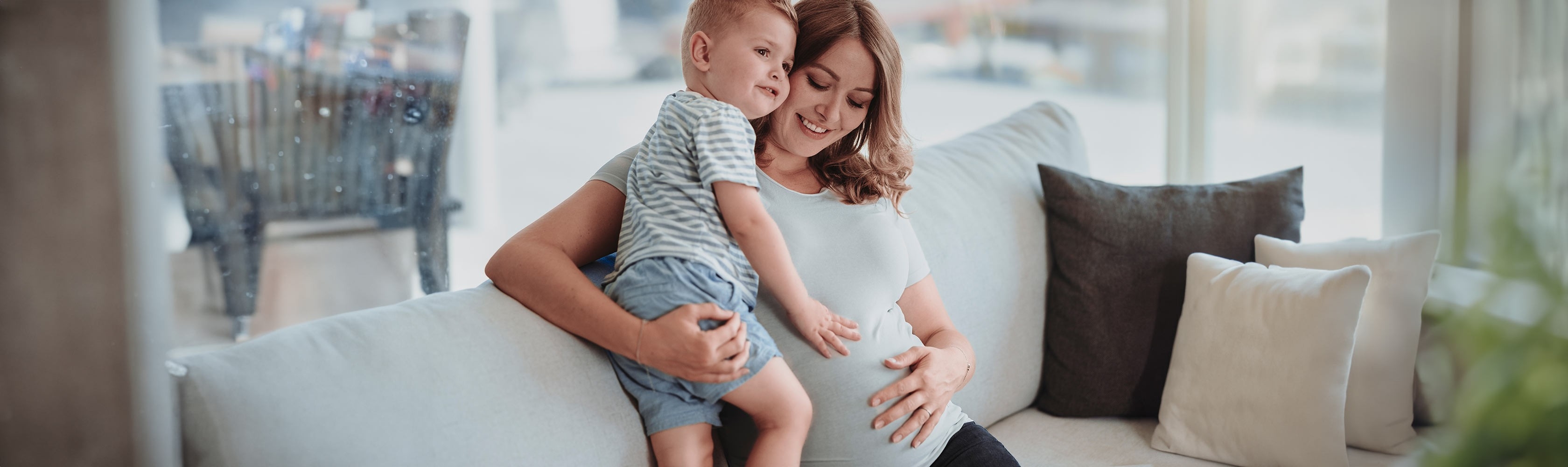 Schwangerschaft und Geburt – Schwangere Mutter hält ihr Kleinkind im Arm und fasst sich an den Bauch