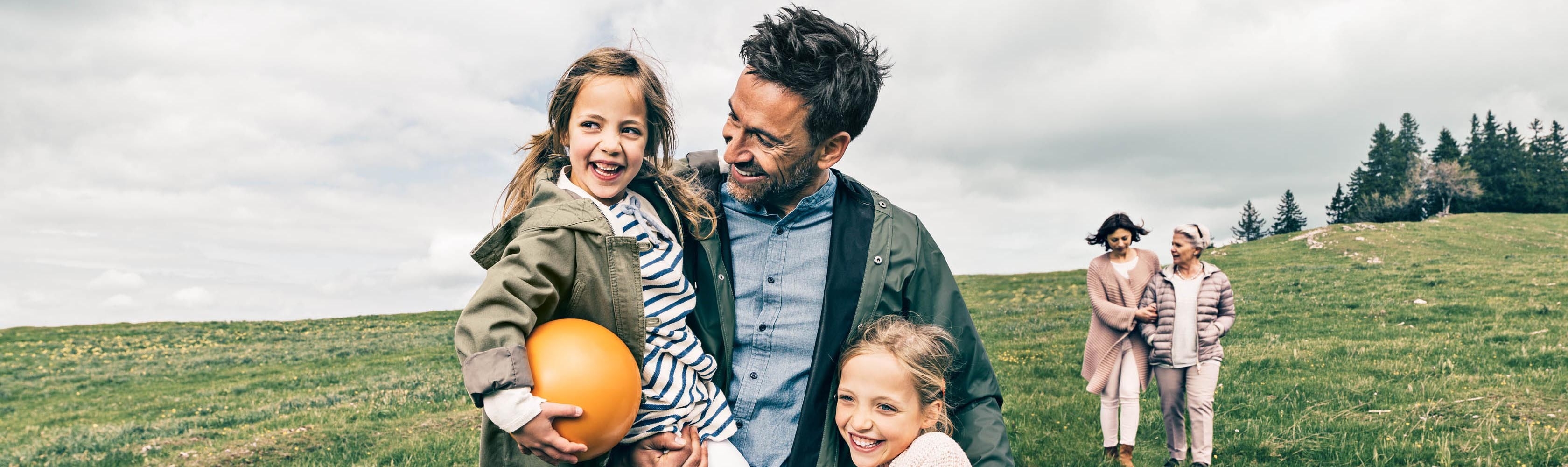Rückruf - Ein Vater hält seine beiden Töchter, eine hält einen CONCORDIA-Ball in der Hand. Im Hintergrund spazieren Mutter und Grossmutter, alle auf einer Wiese