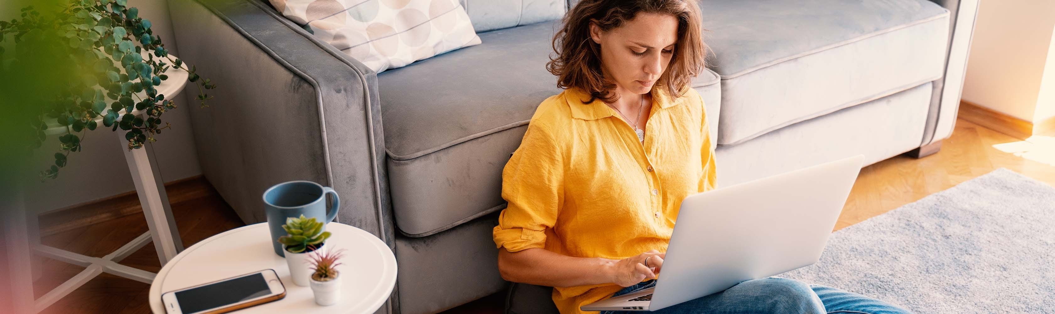 Eine Frau sitzt in ihrem Wohnzimmer mit dem Laptop.