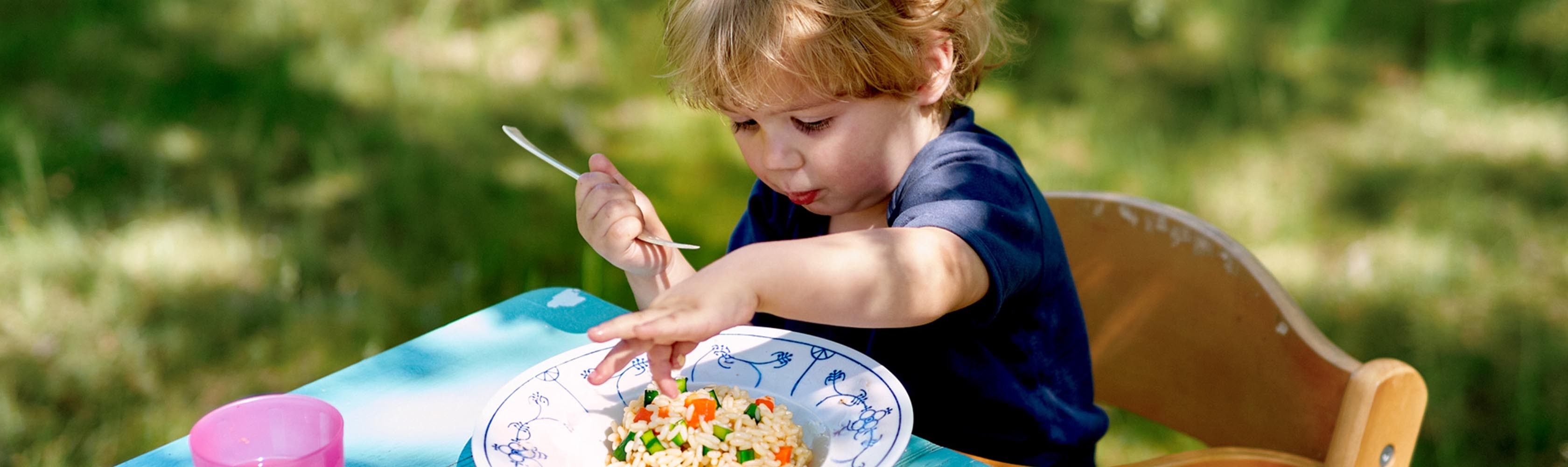 Ein kleiner Junge isst Risotto.