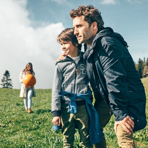 Knabe mit Vater. Im Hintergrund steht die Mutter