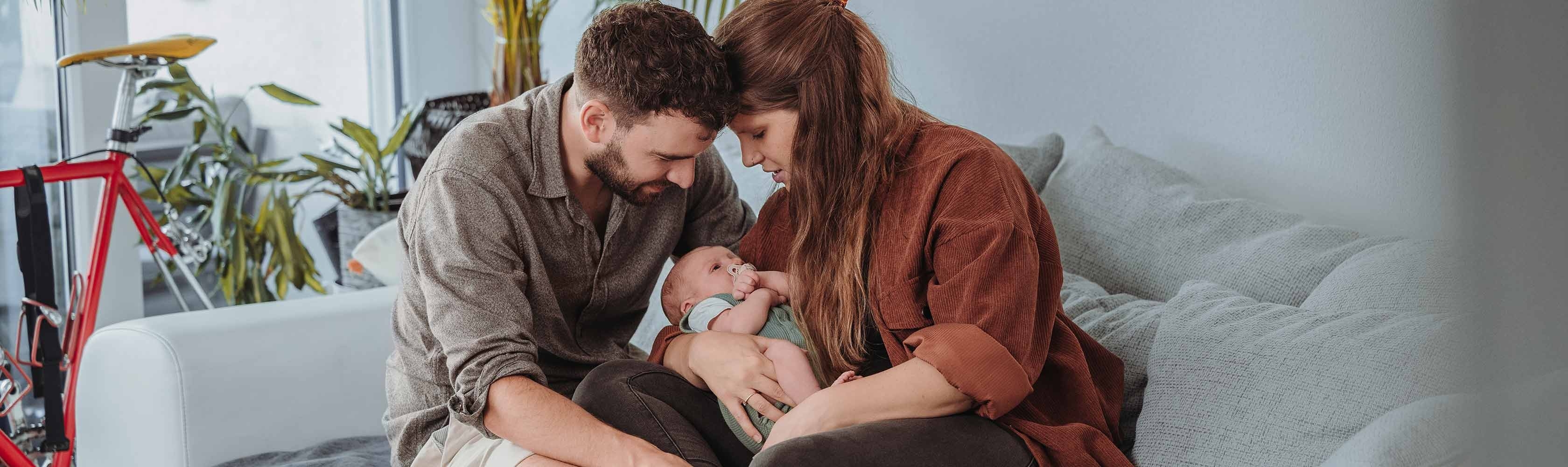 Kooperation - junge Familie mit Baby auf dem Sofa im Wohnzimmer