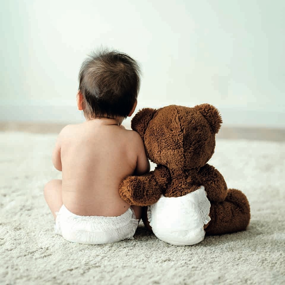 Windelabo Wettbewerb - Ein Baby sitzt neben einem Teddy auf dem Teppich, beide tragen eine Windel