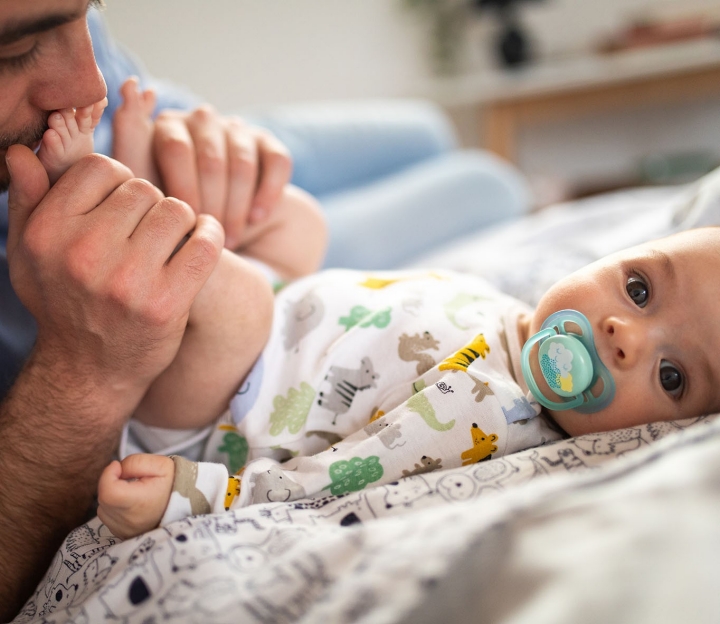 Mein Kind - Baby liegt auf dem Rücken und der Vater schaut sein Kind an.