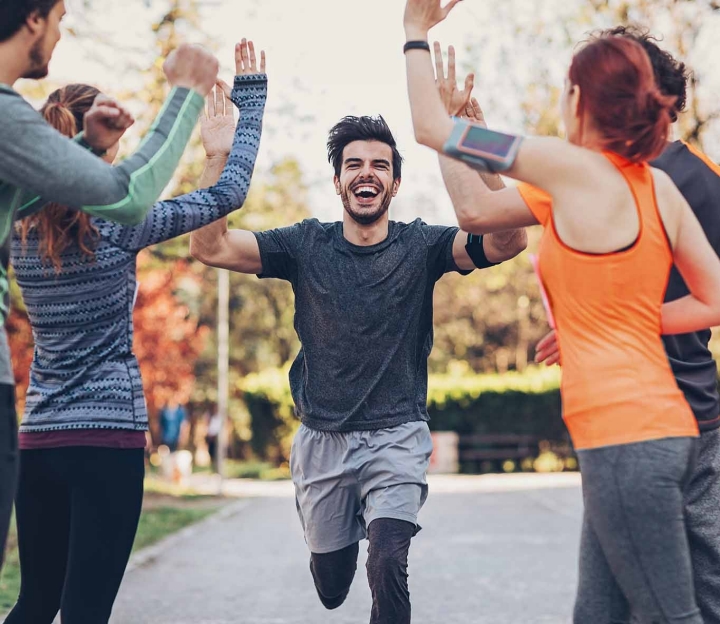 A runner high-fiving with 4 others. All are standing in an avenue of trees in sportswear.