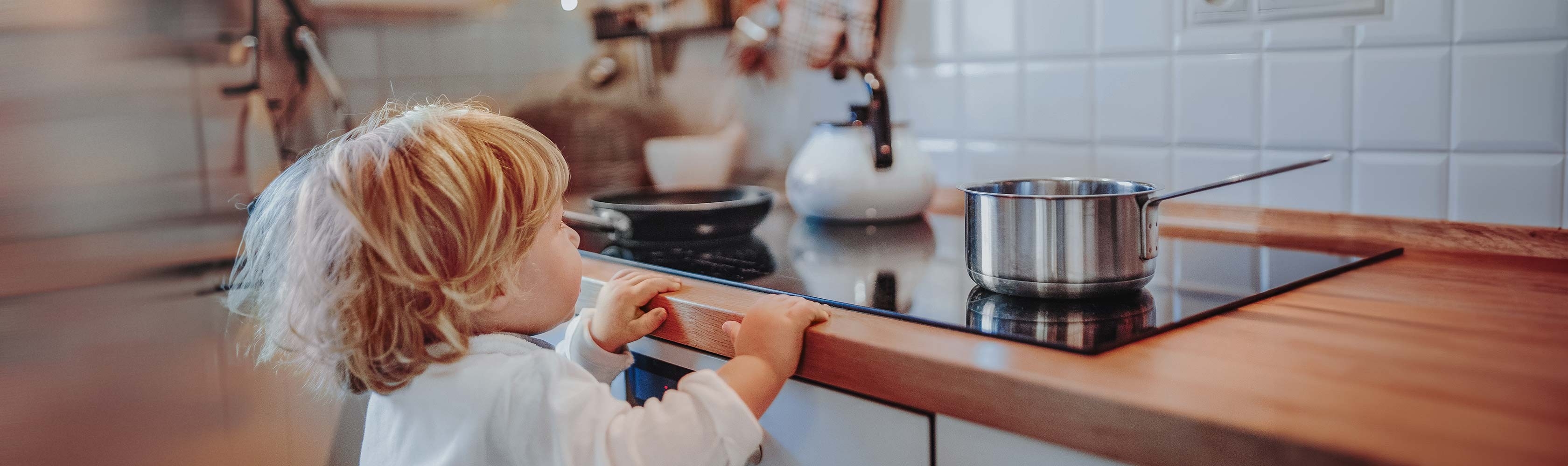Verbrennungen - Kleinkind steht gefährlich nahe am Herd, während kochendes Wasser auf dem Herd steht.