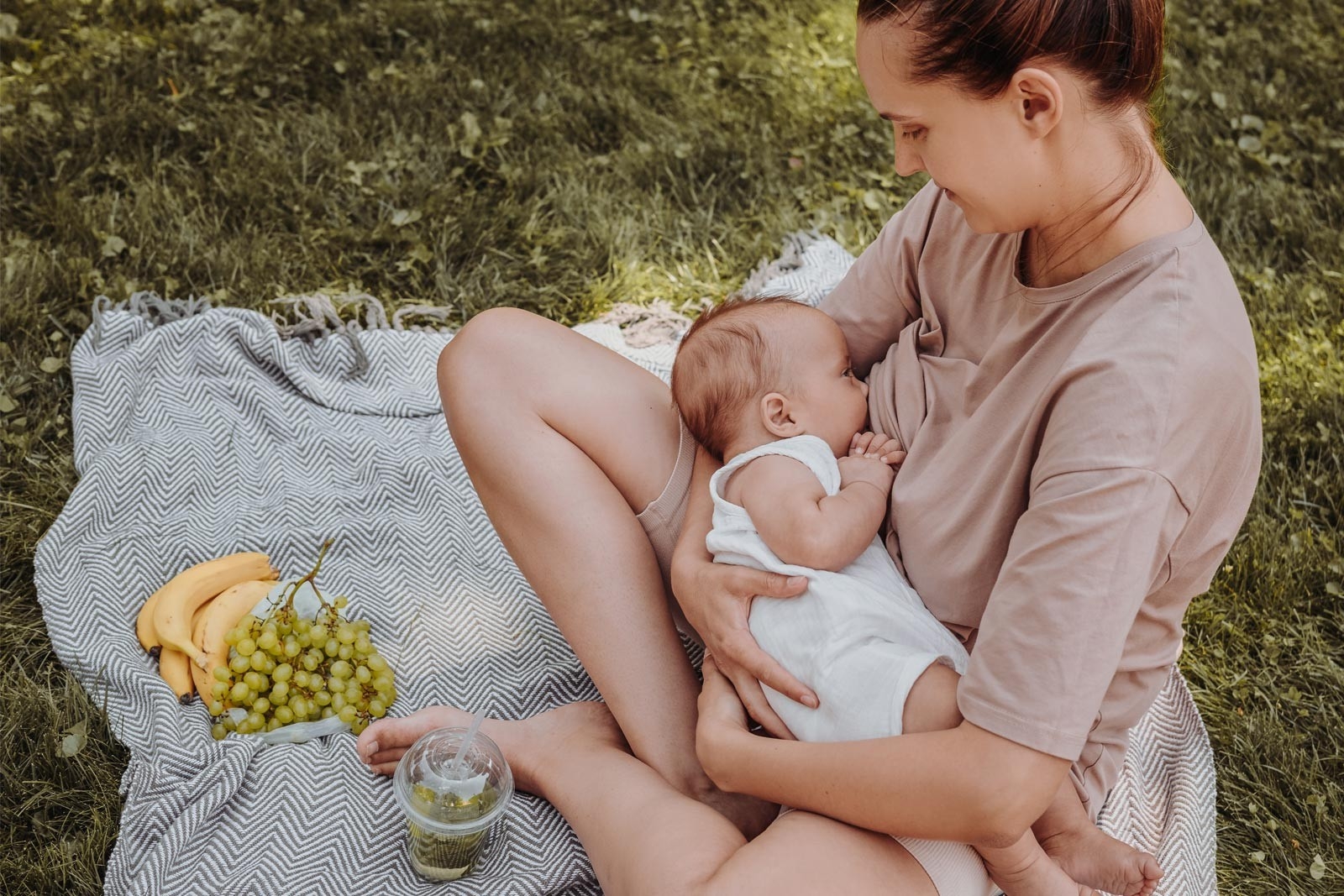 Breastfeeding and breast milk – a woman is sitting in a garden on a picnic blanket and breastfeeding her baby