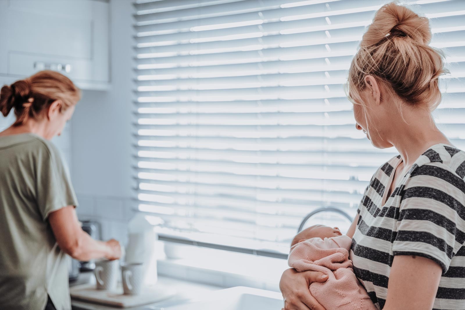 The postpartum period – a mother holds her baby while another woman makes tea for her