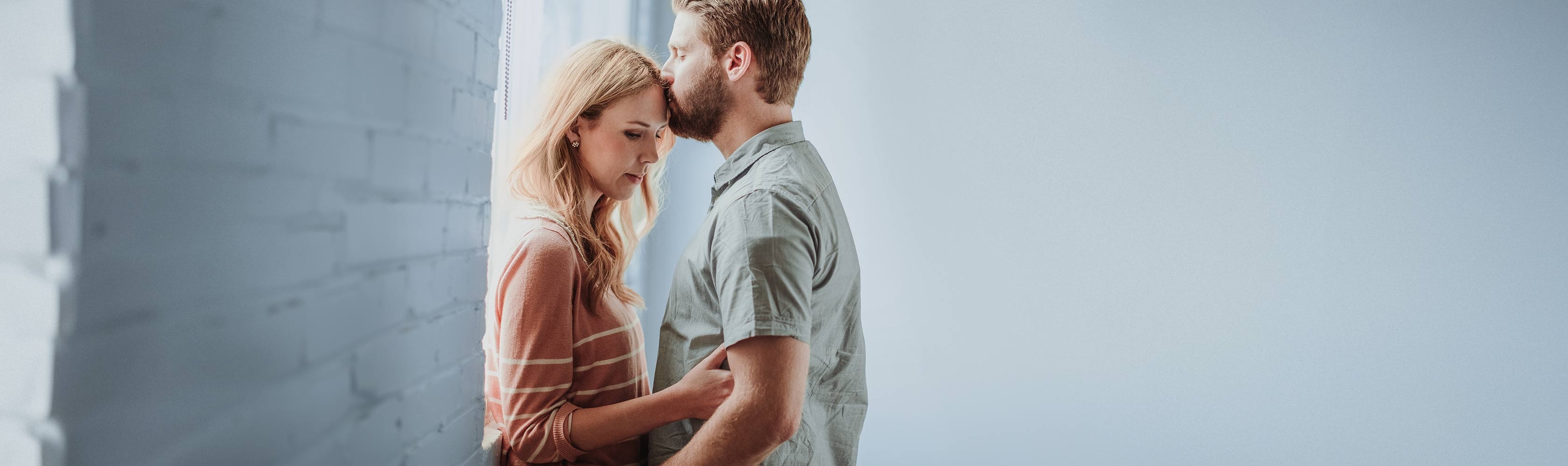 Problems getting pregnant – a man kisses a woman on the forehead; both have sad facial expressions
