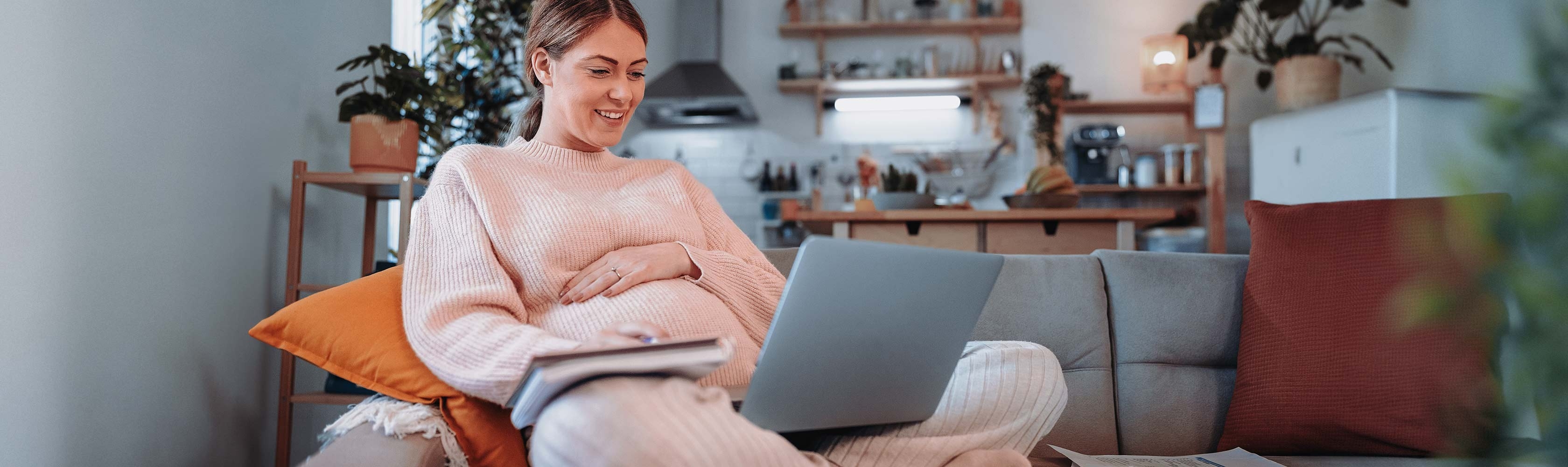 Health insurance and maternity – a pregnant woman sits on the couch with her laptop and paperwork