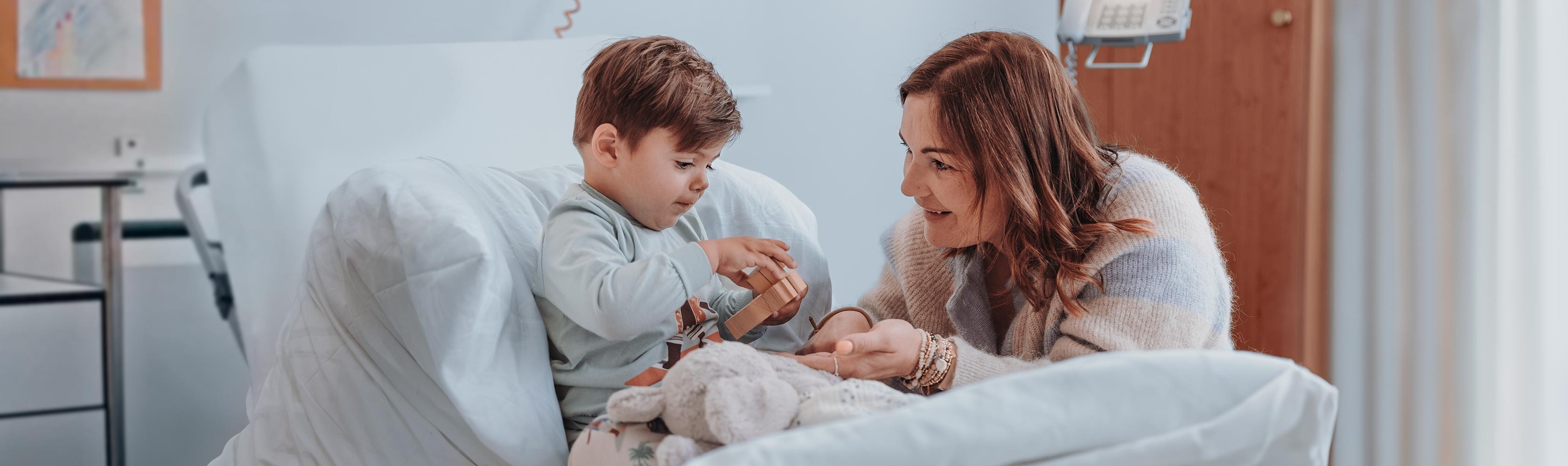 Rooming in – a mother is playing with her son on the bed in the hospital room