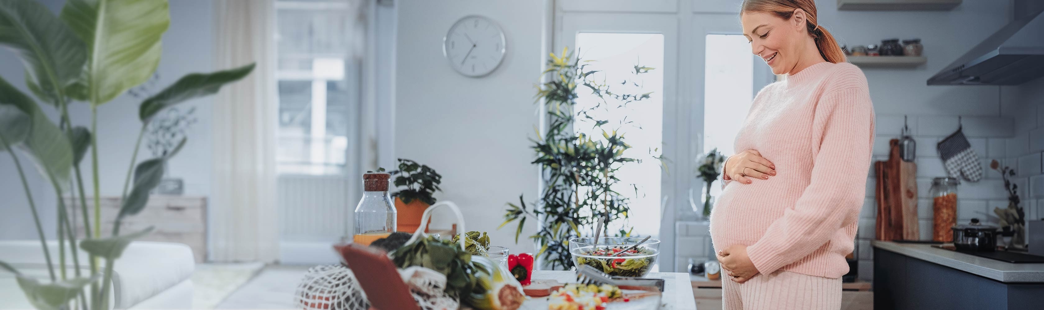 Pregnancy and gaining weight – a pregnant woman stands in the kitchen and cooks herself a healthy meal.
