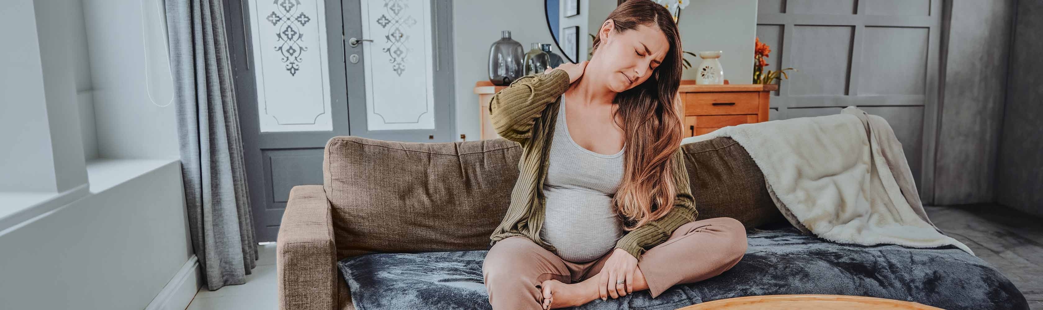 Back pain during pregnancy – a pregnant woman sits on the sofa, suffering from back pain