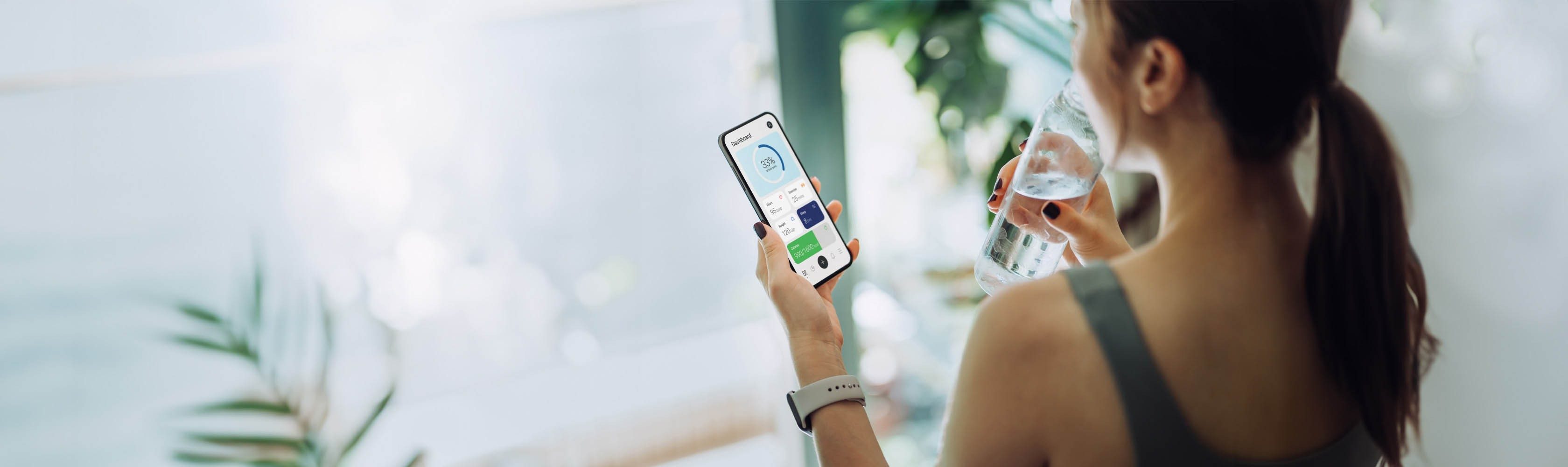 Applications santé - Une jeune femme sportive consulte l'application fitness sur son smartphone tout en buvant à une bouteille d'eau.