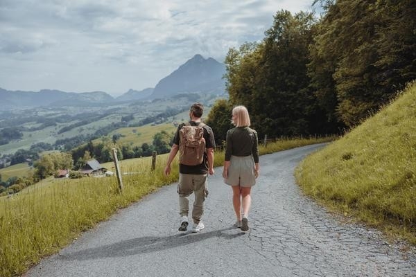 Offres Active - Un couple se promène sur une route de campagne asphaltée avec vue sur des prairies vertes et des montagnes en arrière-plan.