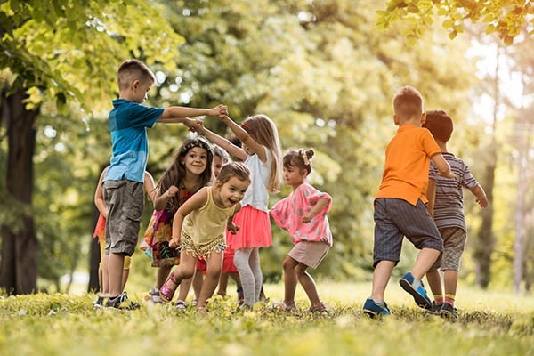 Pro Juventute - Plusieurs enfants jouent joyeusement ensemble à l'extérieur par temps ensoleillé sur une prairie.