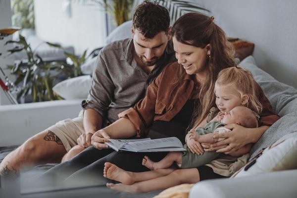 LetsFamily - Un couple de parents est assis sur le canapé avec un bébé et regarde ensemble une tablette - une scène familiale dans le salon.