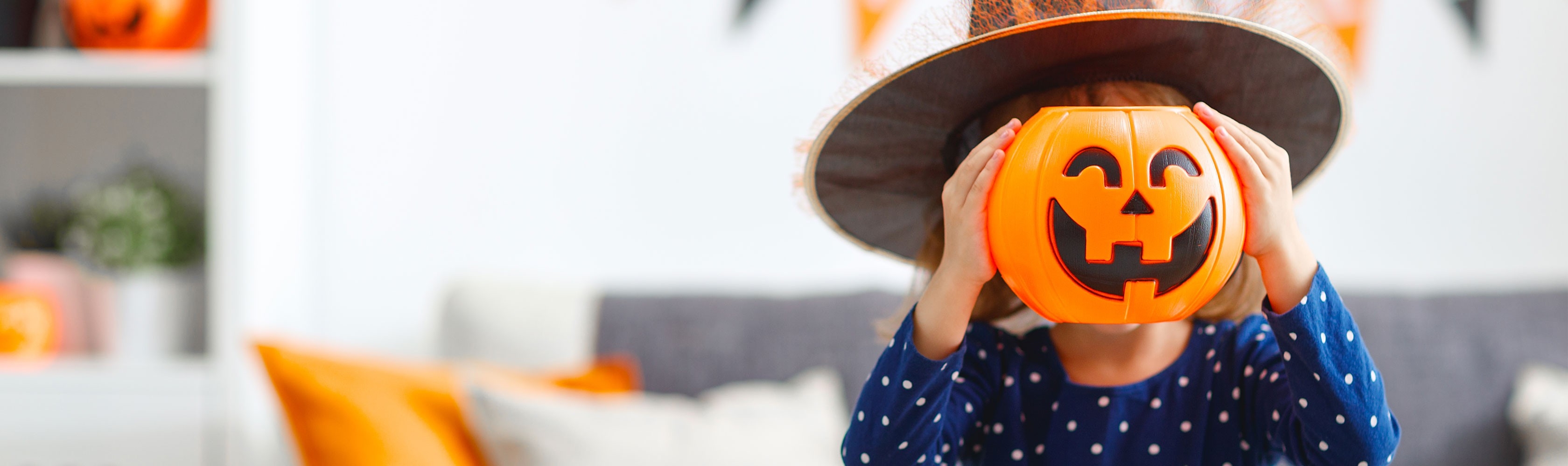 Halloween - ein Kind als Hexe verkleidet hält einen geschnitzten Kürbis vor das Gesicht