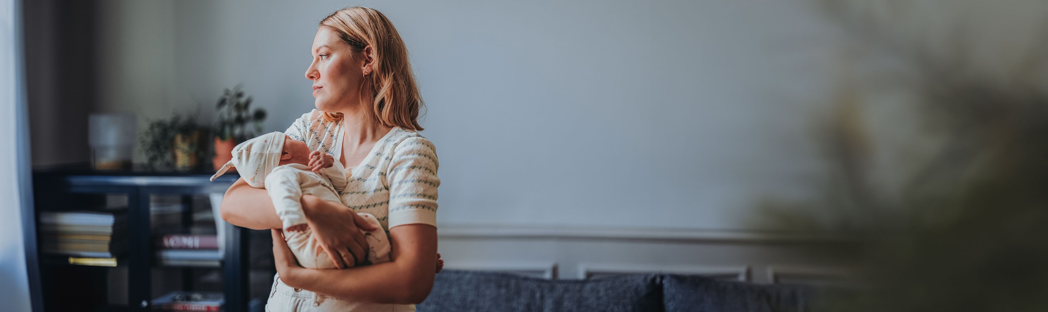 Dépression post-partum - une maman tient son bébé dans les bras et regarde dans le vide.