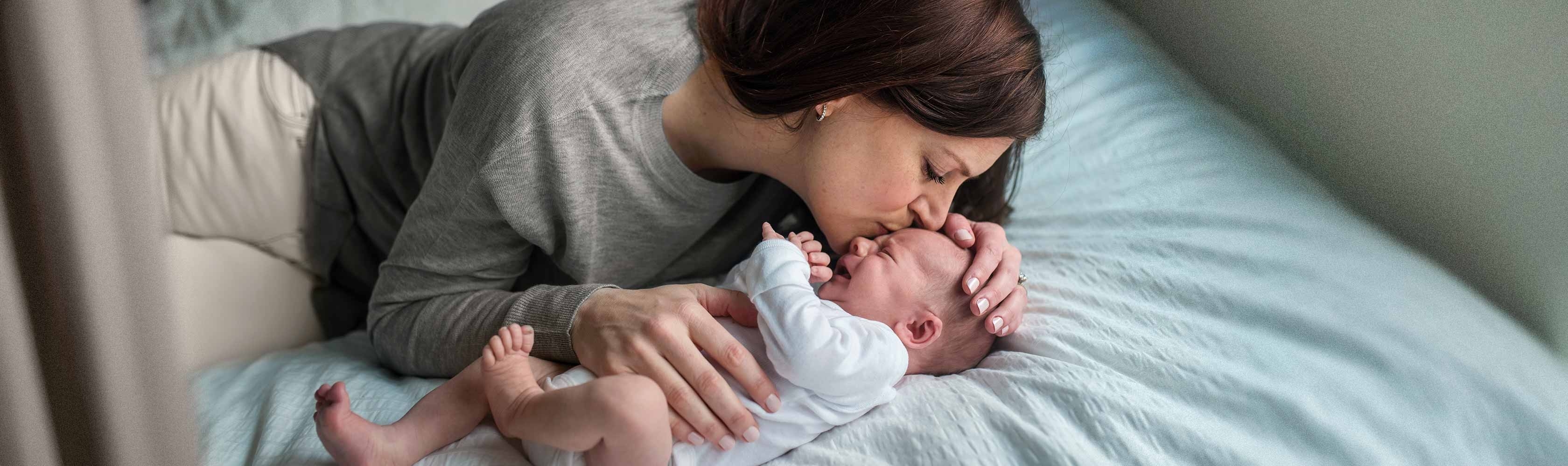 Bébé qui pleure: une maman embrasse tendrement son bébé qui pleure sur le front.
