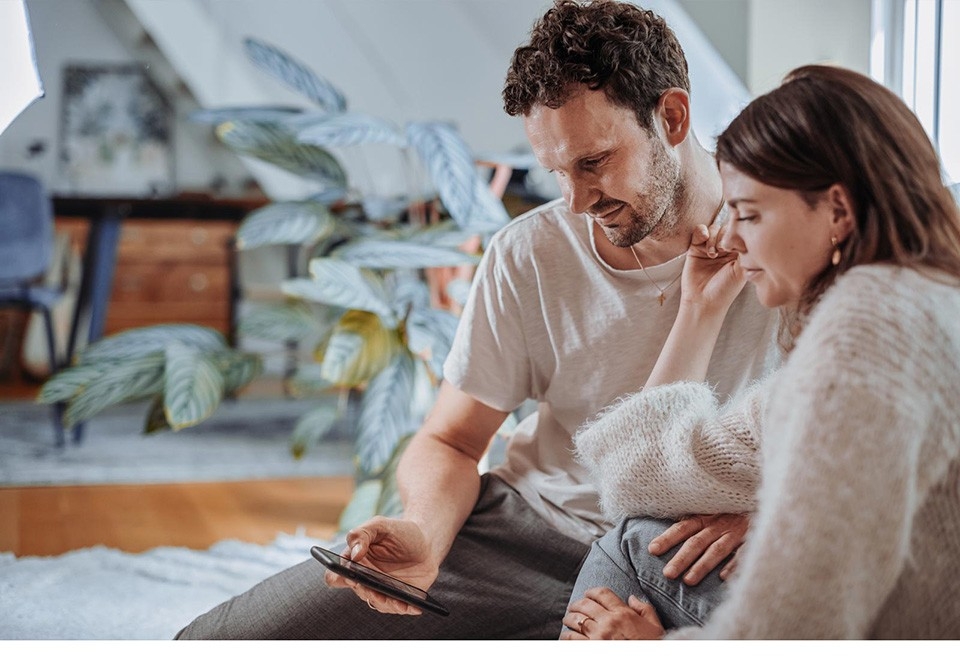 Avoir un bébé: un couple est assis sur le canapé et consulte le suivi du cycle menstruel sur le smartphone.