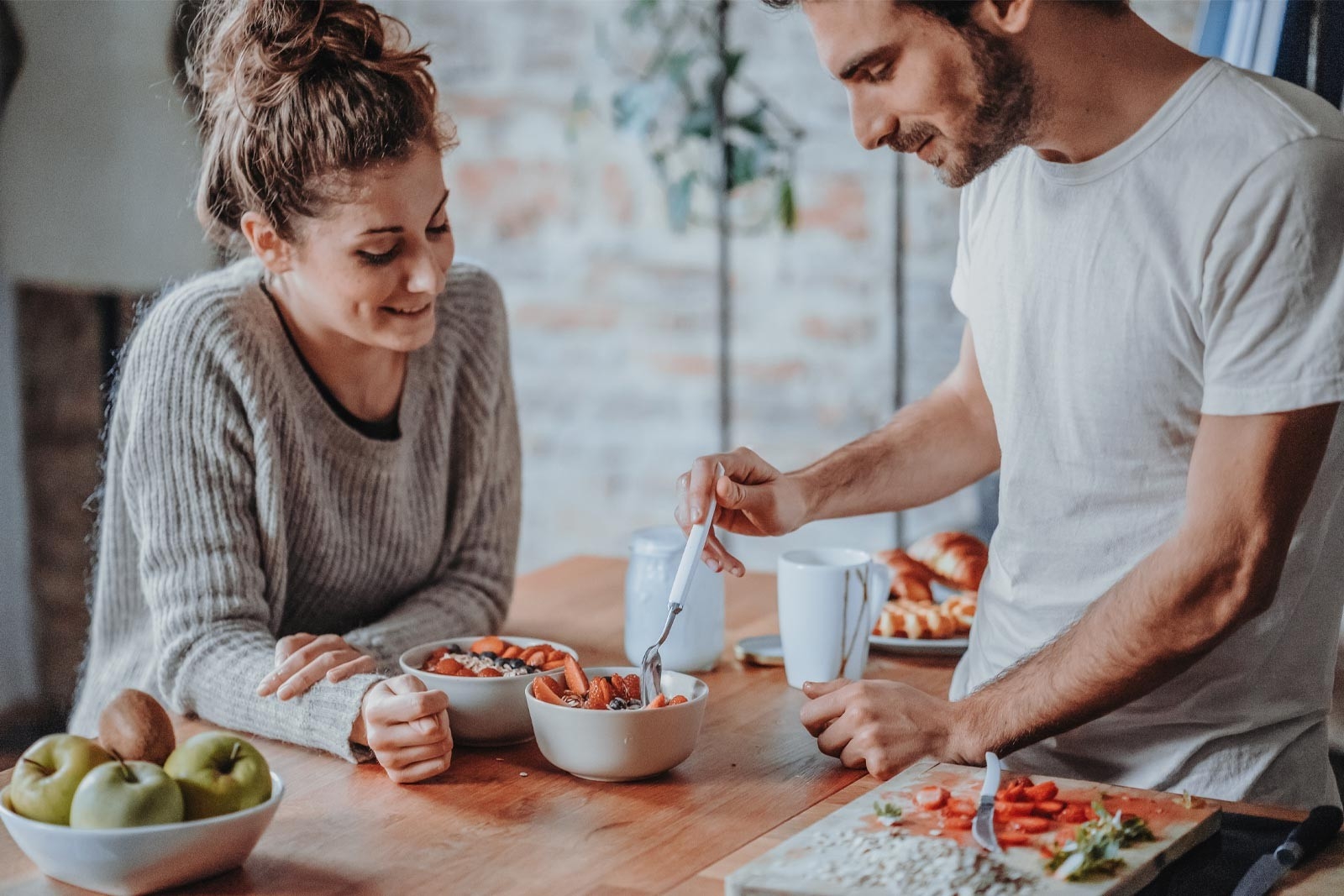 Avoir un bébé: un couple mange un bowl nourrissant avec des fruits à la table de la cuisine.