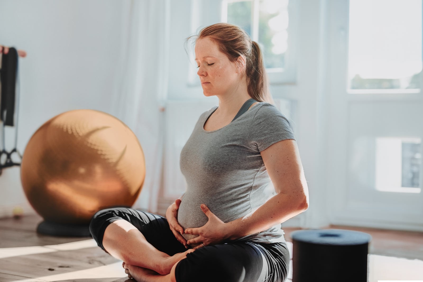 Sport durant la grossesse - une femme enceinte est assise en tailleur sur le sol et se tient le ventre