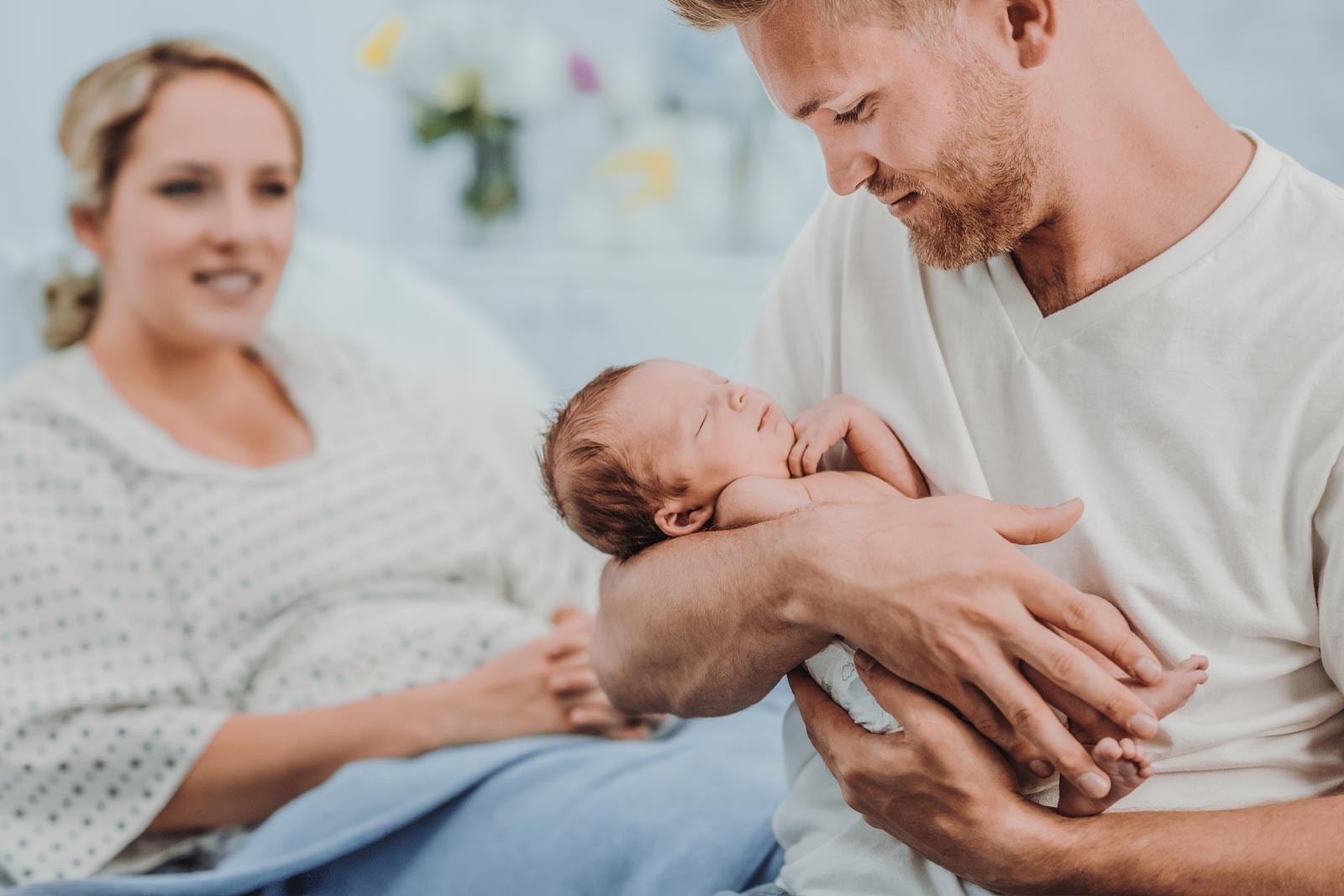 Rooming-in: une maman est couchée dans un lit d’hôpital. Le papa tient le bébé dans ses bras.