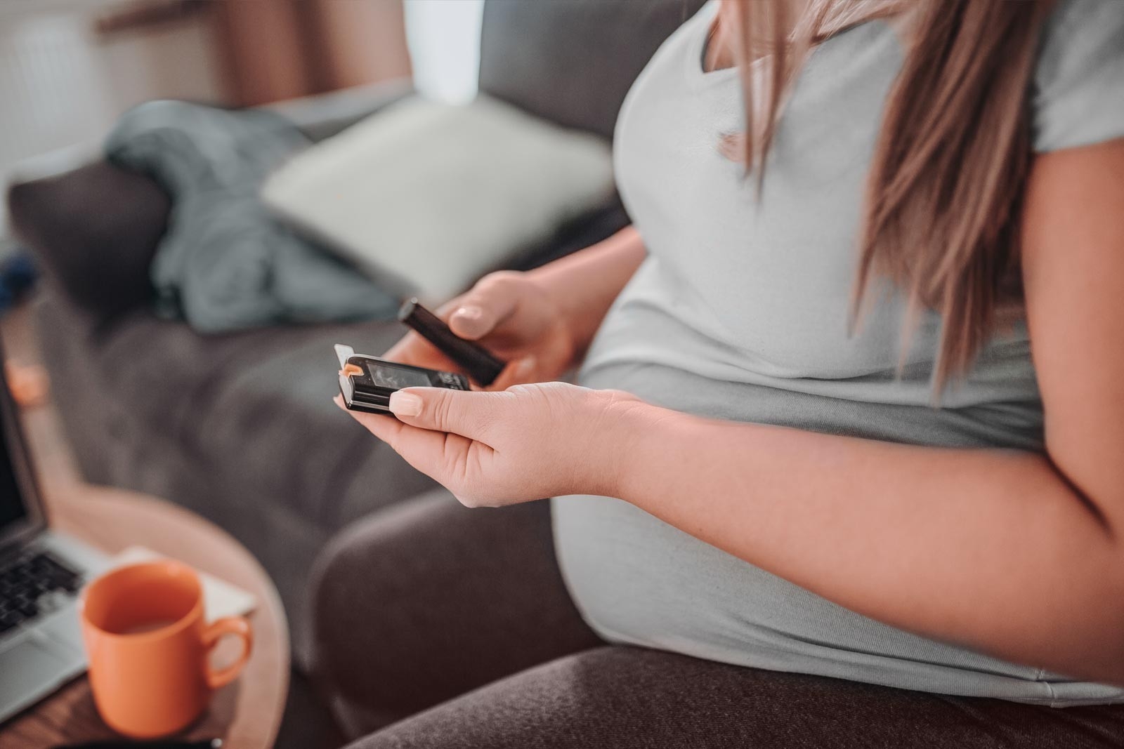 Diabète gestationnel: une femme enceinte est assise sur son canapé et consulte son glucomètre.