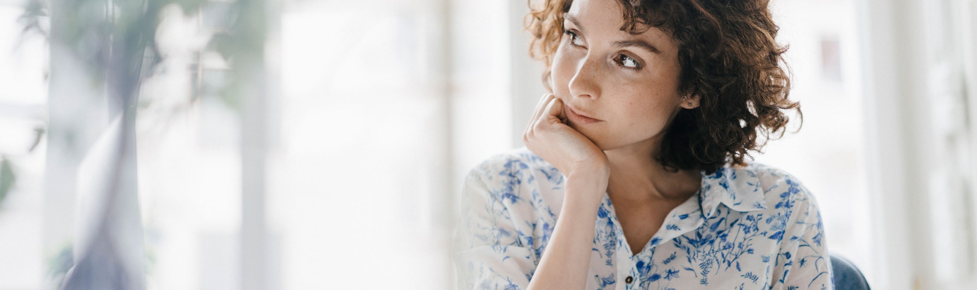 Une femme regarde dans le vide, perdue dans ses pensées, un téléphone portable à la main.