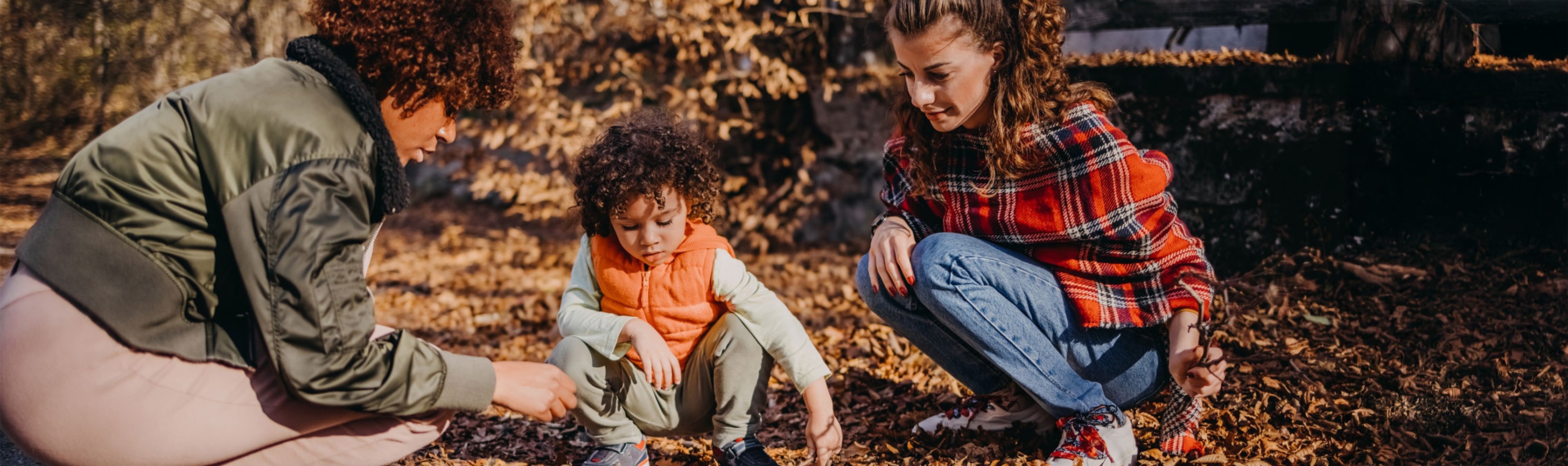 Deux femmes sont accroupies dehors avec un enfant dans les feuilles mortes.