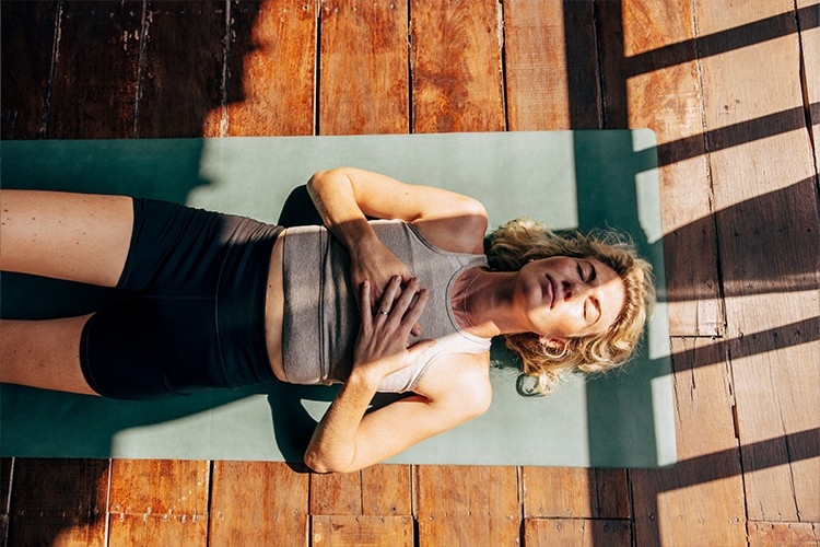 Une femme est allongée sur un tapis de yoga et essaie de se détendre.