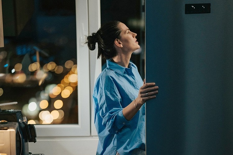Une femme ouvre le réfrigérateur dans l'obscurité et regarde autour d'elle.