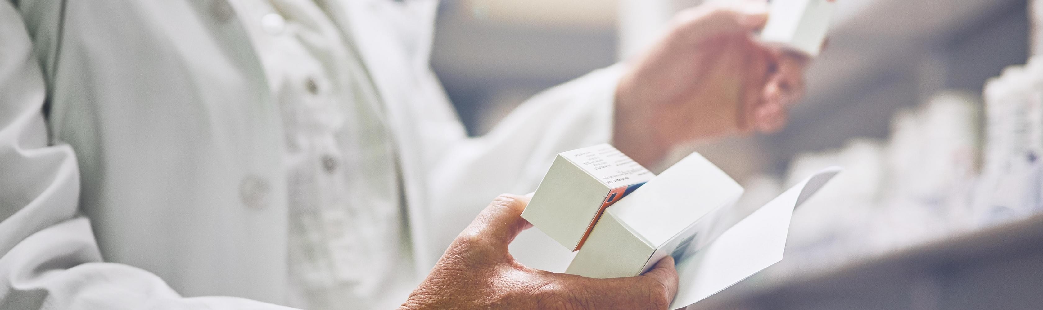 Une personne spécialisée tient plusieurs boîtes de médicaments dans ses mains.