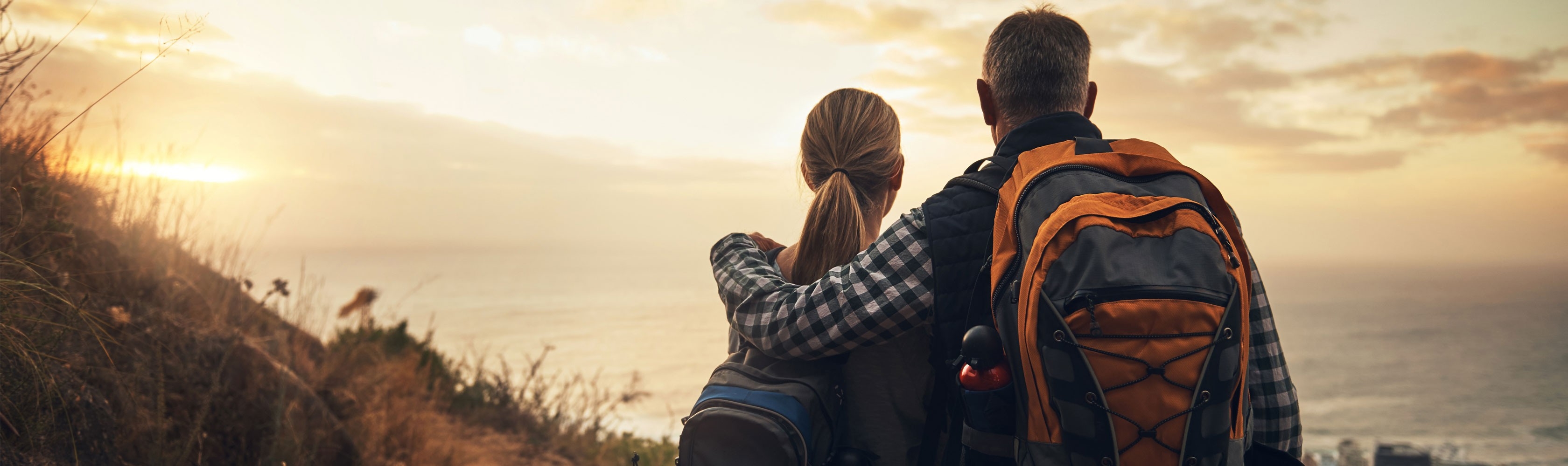 Une femme et un homme font le tour du monde. Ils portent des sacs à dos, se tiennent debout sur une montagne et profitent de la vue.
