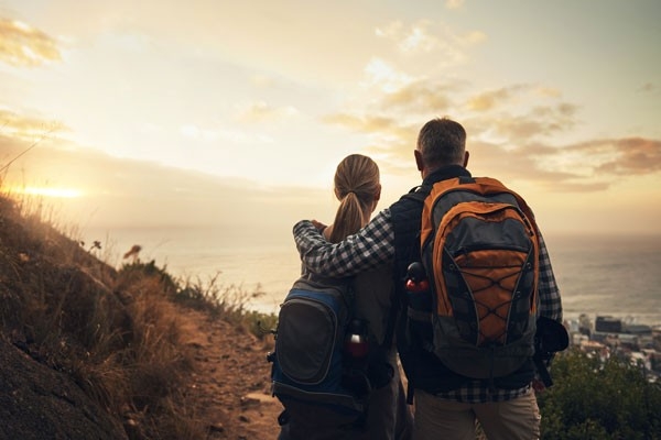 Une femme et un homme font le tour du monde. Ils portent des sacs à dos, se tiennent debout sur une montagne et profitent de la vue.