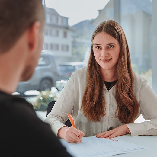 Une jeune conseillère en assurance est assise face à un client intéressé et lui présente, sans engagement, les solutions d’assurance les mieux adaptées à ses besoins.