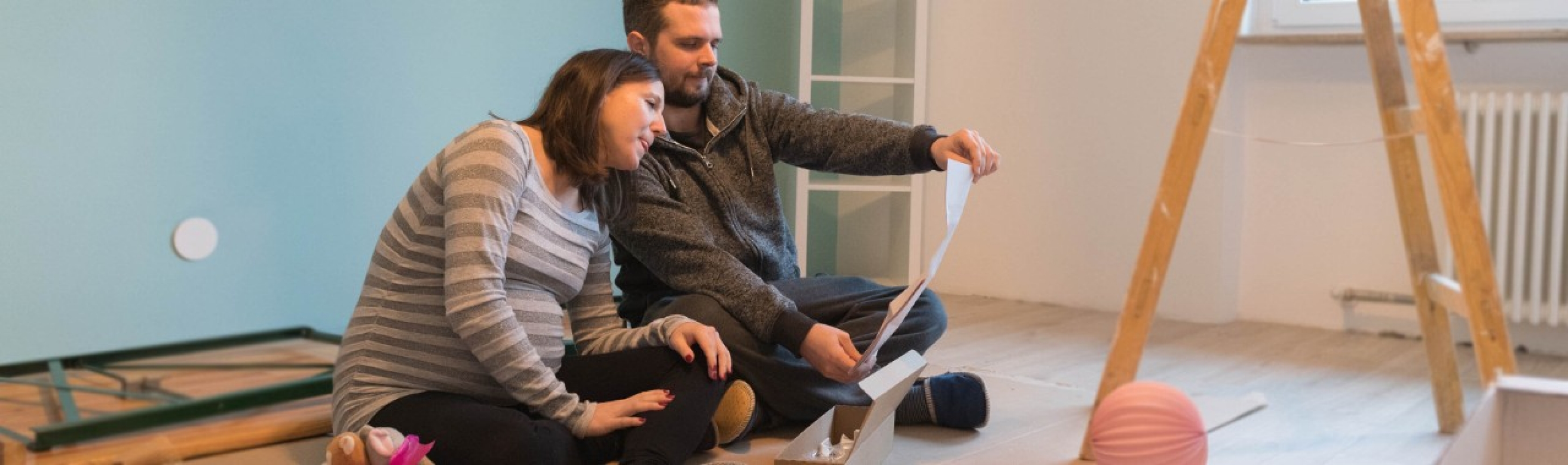 Couple enceinte assis par terre dans la chambre d'enfant et lisant un mode d'emploi.