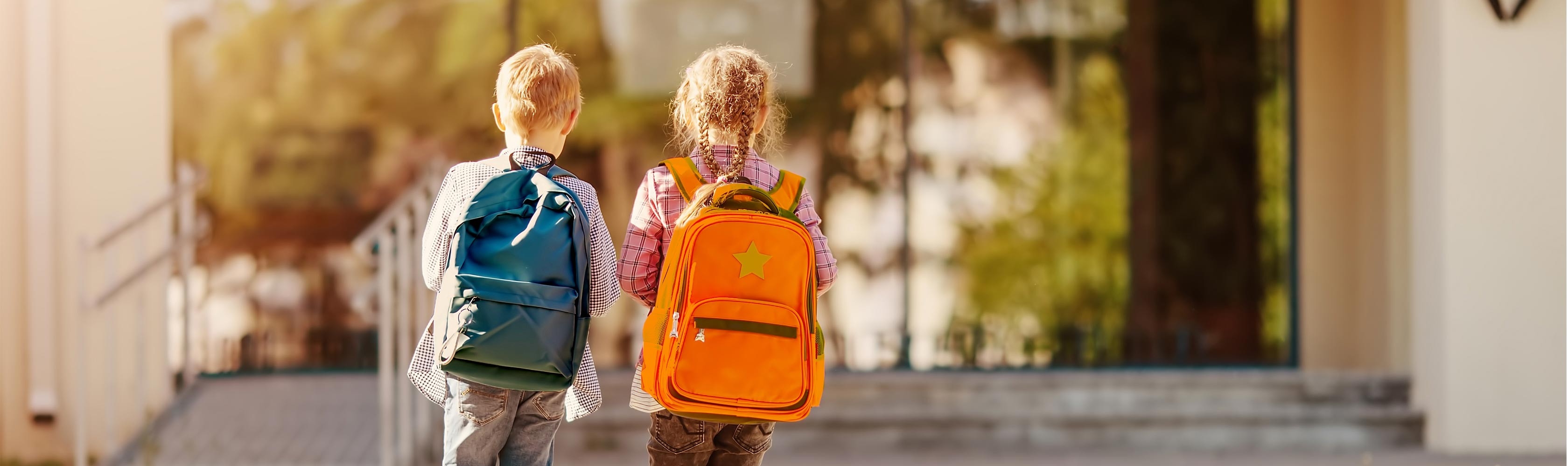 Sicherheit Schulweg – zwei Kinder laufen zur Schule mit farbigen Rucksäcken