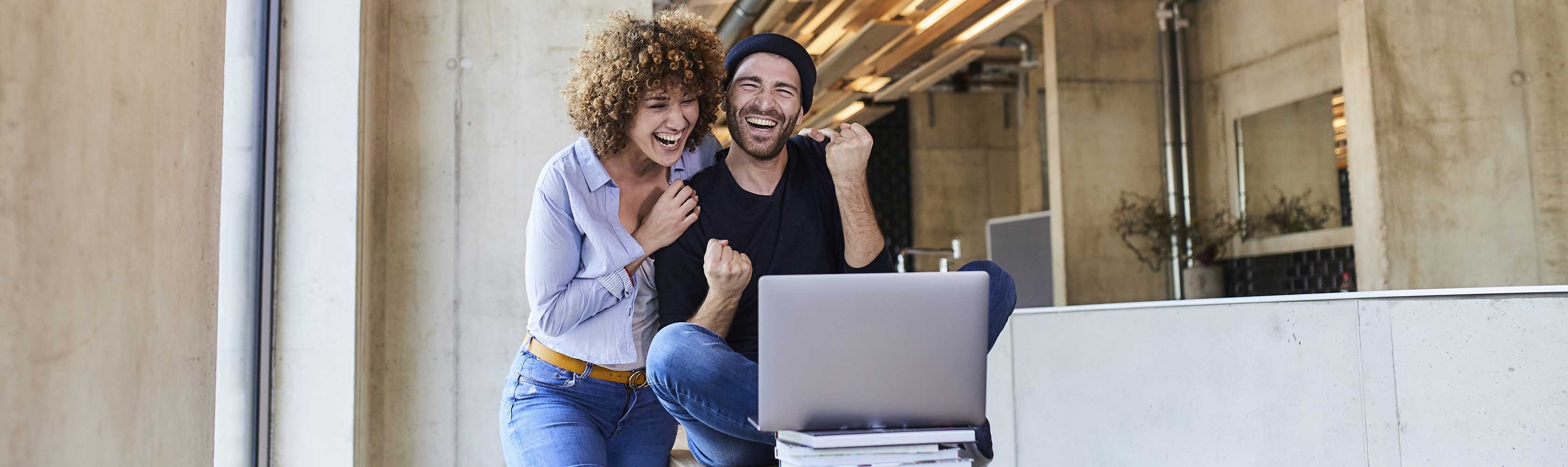 Un uomo e una donna guardano insieme un LapTop in un interno e sono felici.