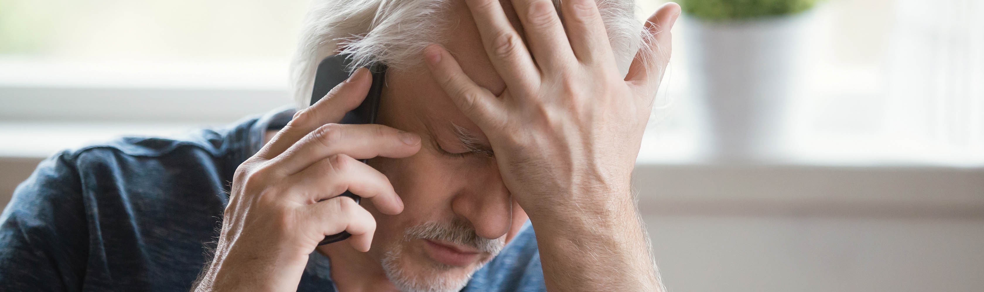 Un uomo soffre di vertigini e non si sente bene. Ha gli occhi chiusi e una mano sulla fronte mentre allerta telefonicamente il numero d emergenza.