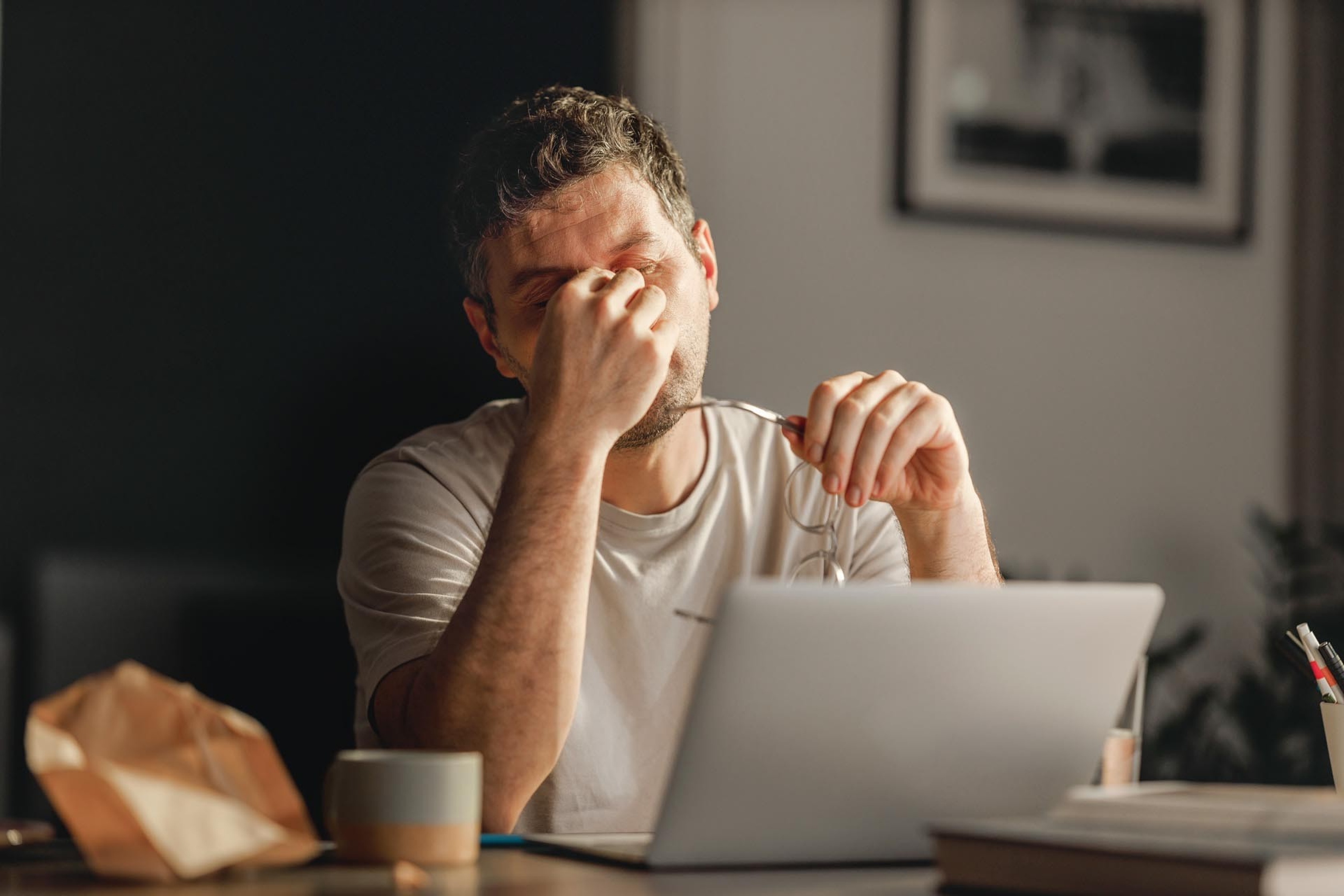 Ein Mann reibt sich die Augen vor dem Laptop