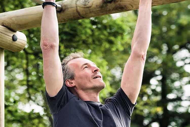 Un uomo di mezza età si allena su un ostacolo del percorso fitness nel bosco